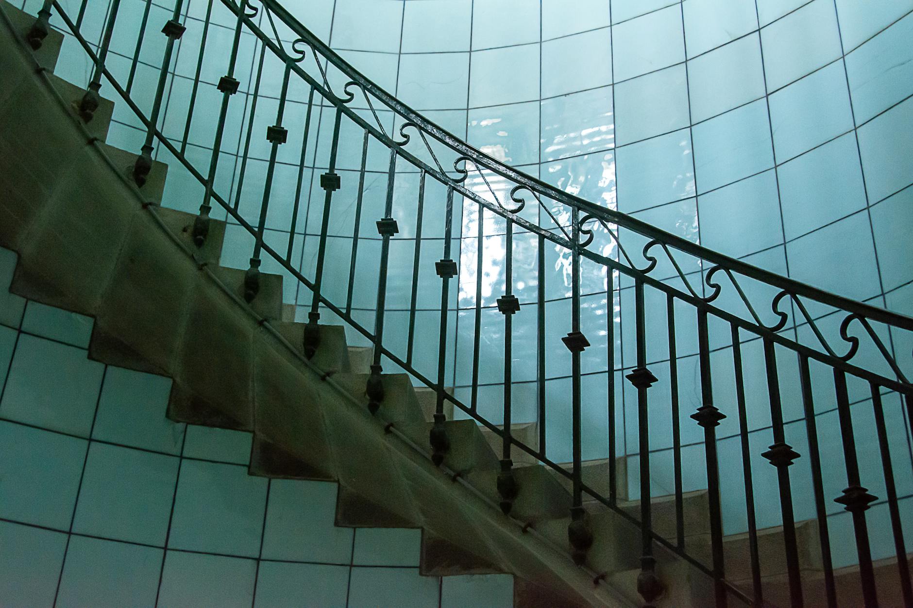 Kręte schody z kutą balustradą przy ścianie z niebieskich płytek