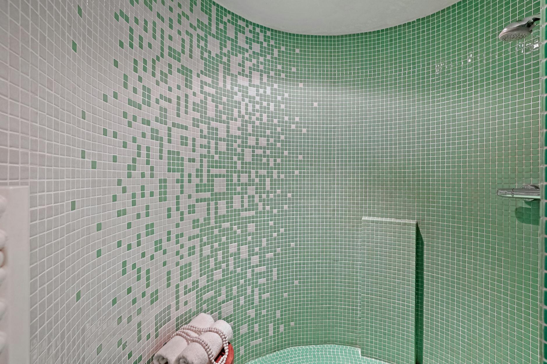 Mała łazienka z zielono-białą mozaiką i zestawem złożonych ręczników