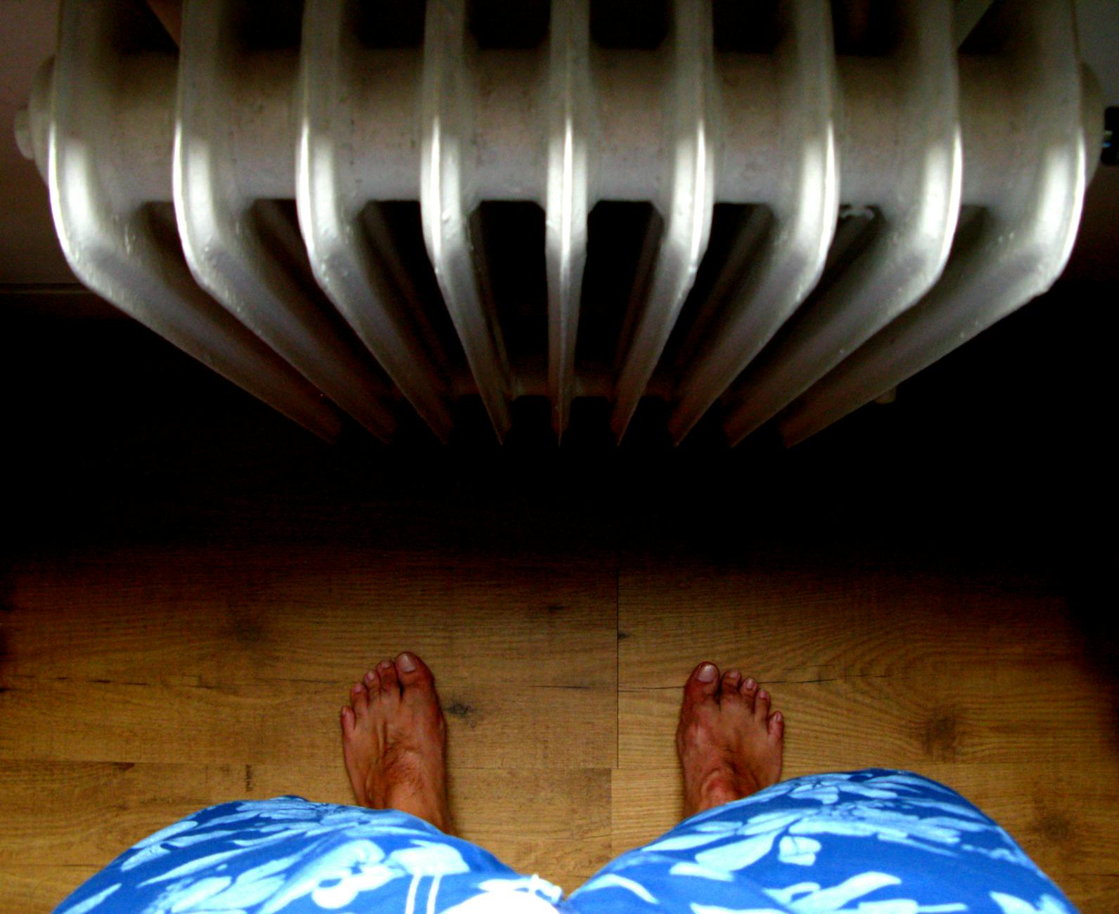 Stopy boso na drewnianej podłodze obok grzejnika centralnego ogrzewania