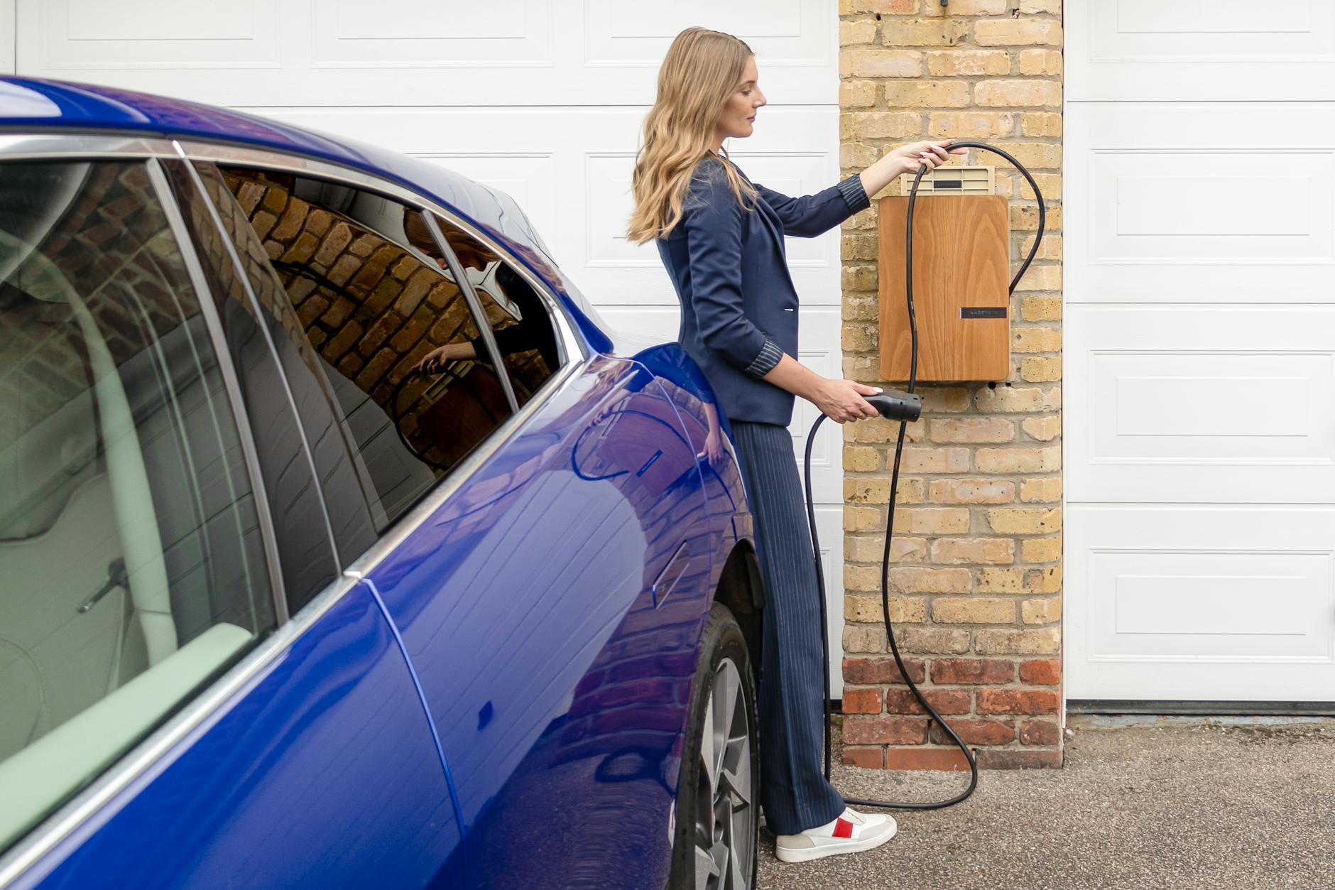 Kobieta ładuje niebieski samochód elektryczny z domowej ładowarki