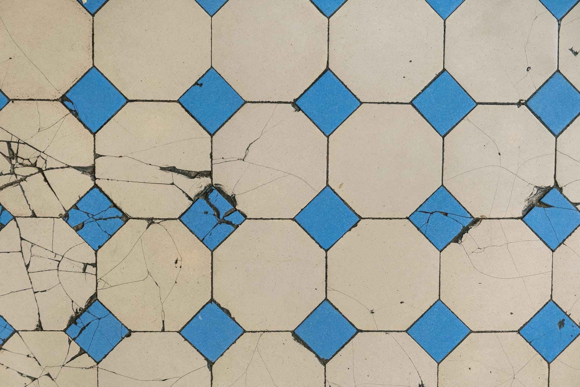 Popękane geometryczne płytki podłogowe z niebieskimi rombami na beżowym tle