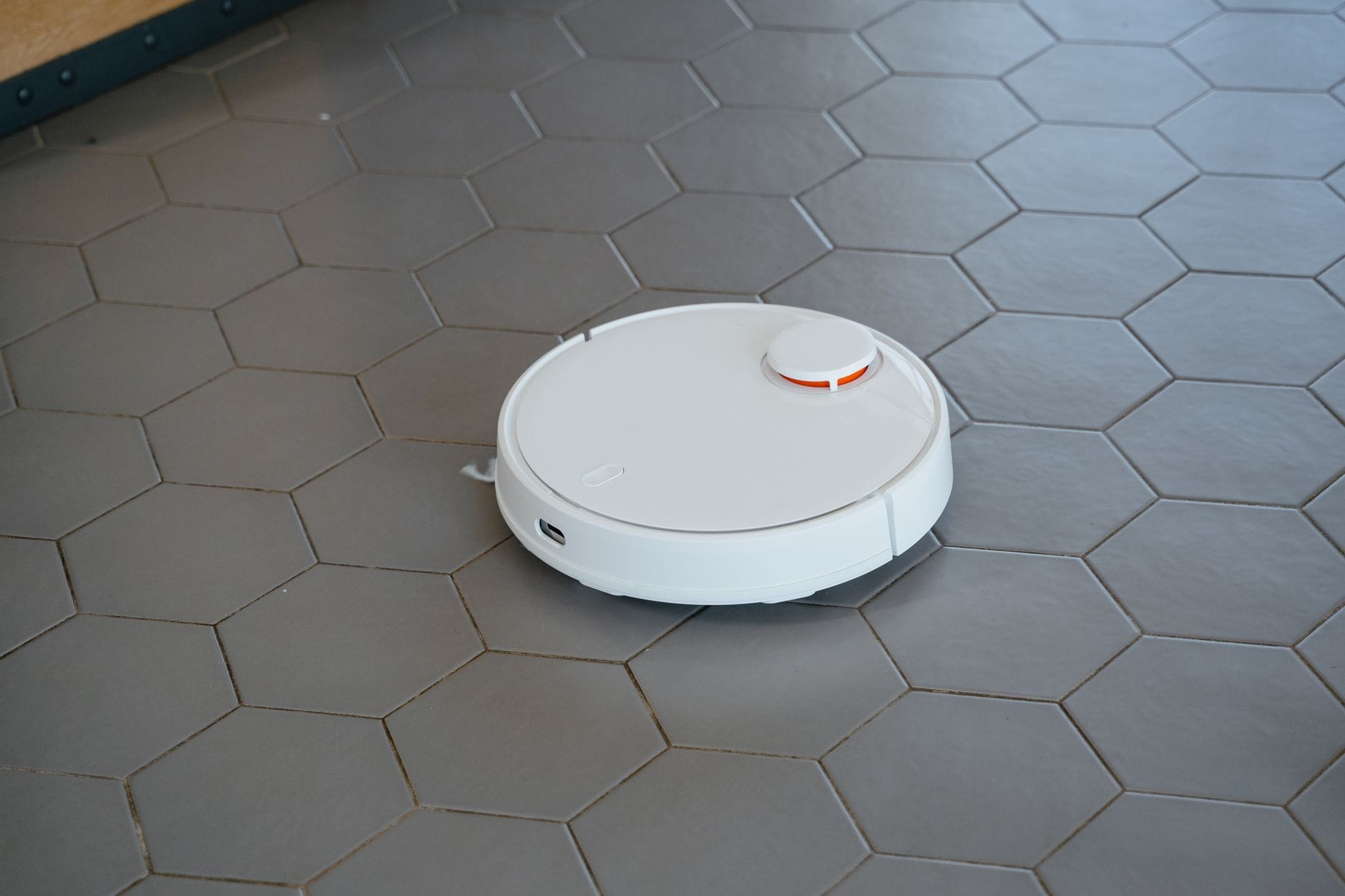 Biały robot odkurzający pracujący na podłodze z heksagonalnego gresu